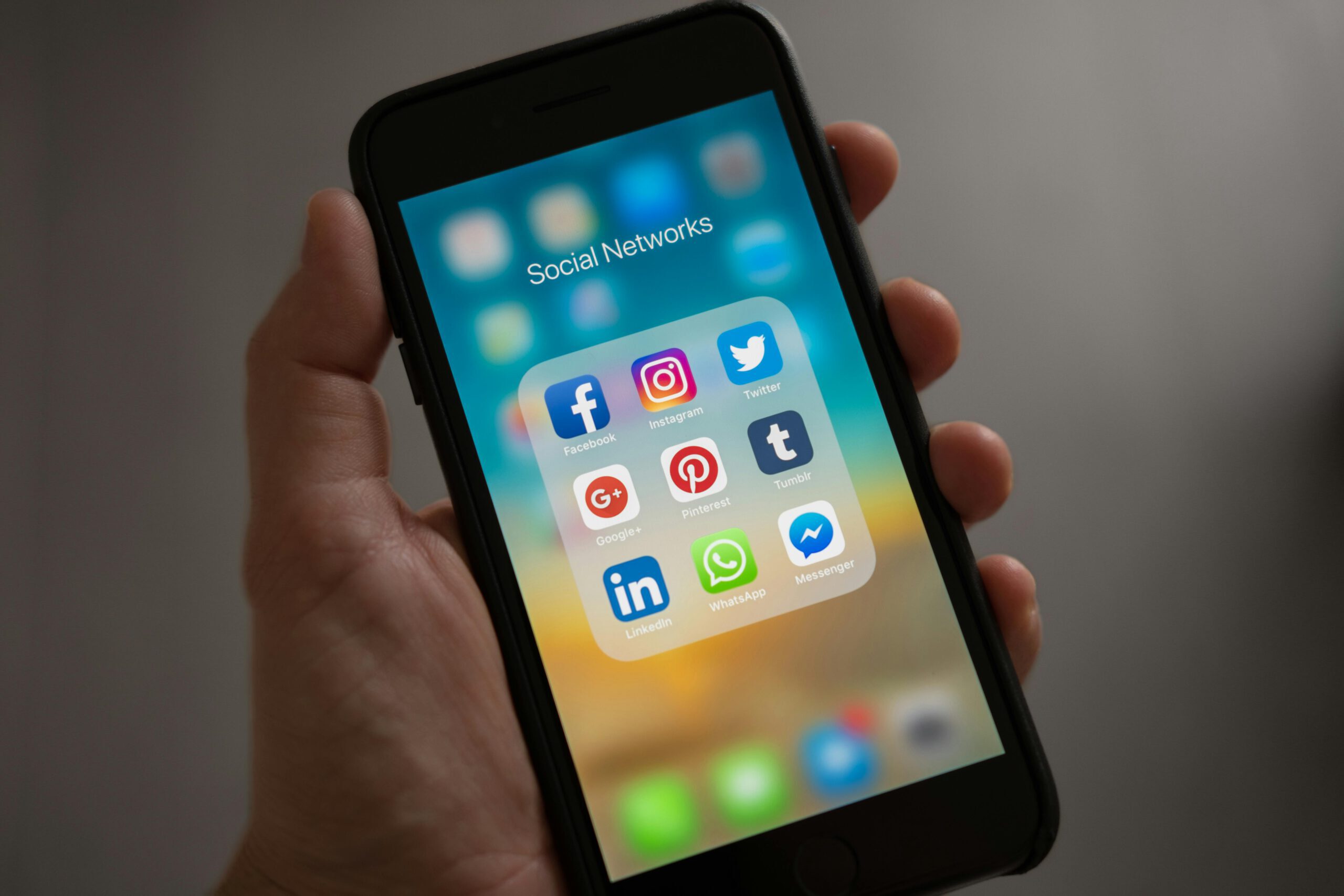 Hand hält Smartphone mit geöffnetem Ordner ‚Social Networks‘, der Apps wie Facebook, Instagram, Twitter, LinkedIn und WhatsApp zeigt
